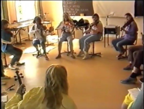 Still picture from the documentary about the 1990’s Ethno available at https://youtu.be/UKhad4-4rbI. Here we can see students sitting in a circle, playing a tune taught by another student. This peer learning pedagogy and format is the same used in 2018’s Ethno.
			