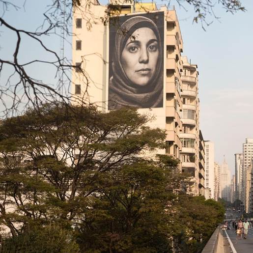 Fotografia de Salsabil Matouk, refugiada s&iacute;ria habitante de S&atilde;o Paulo, realizada em 2018 como parte do projeto Giganto, da fot&oacute;grafa Raquel Brust, na fachada lateral da Casa do Estudante da S&atilde;o Francisco, que ladeia o Minhoc&atilde;o.[10]